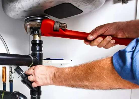 Plumber tightening a sink drain connection with a pipe wrench