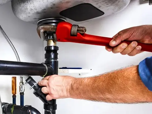 Plumber loosening a clogged sink drain with a pipe wrench