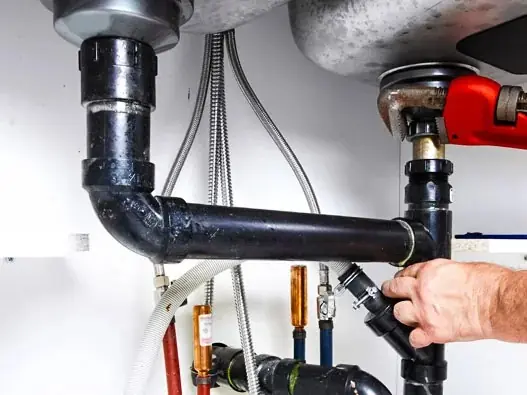 Plumber repairing leaking drain pipes under a kitchen sink